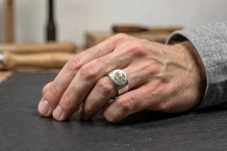 Chevalière homme en argent gravée portée à la main, posée sur une surface en ardoise avec détail du monogramme
